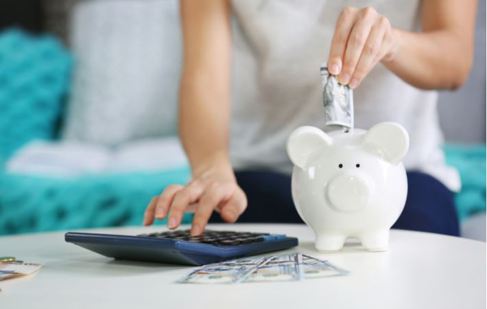 woman putting money into a piggy bank and using a calculator