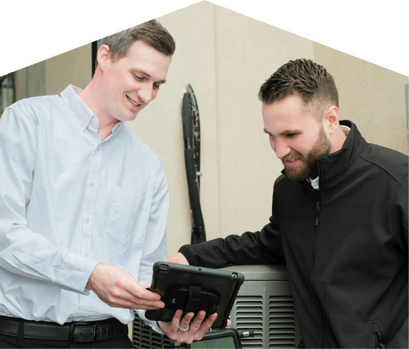 A Mr. Furnace technician in a white shirt shows service details on a tablet to a smiling client in a black jacket, standing beside an AC unit outside a beige building. A Mr. Furnace technician in a white shirt shows service details on a tablet to a smiling client in a black jacket, standing beside an AC unit outside a beige building.