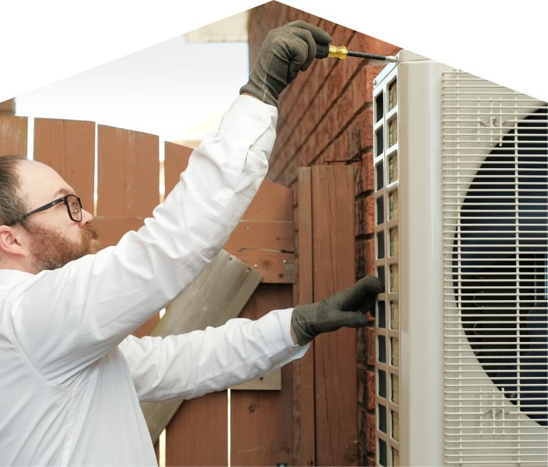 Mr. Furnace service personnel working on an AC condenser, using a screwdriver to secure the unit’s panel outdoors beside a wooden fence. Mr. Furnace service personnel working on an AC condenser, using a screwdriver to secure the unit's panel outdoors beside a wooden fence.
