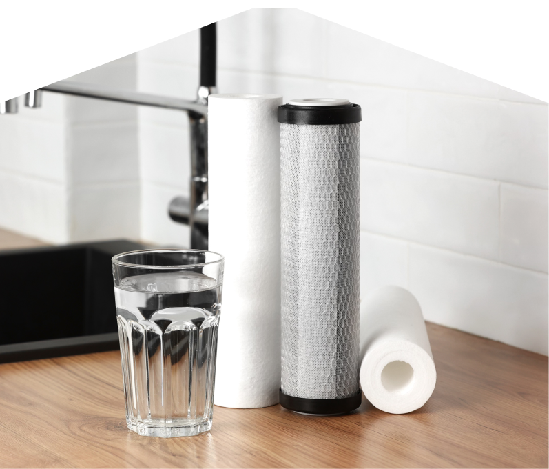 Set of Mr. Furnace water filtration cartridges placed beside a clear glass of water on a kitchen countertop, with a sink and modern faucet in the background. Set of Mr. Furnace water filtration cartridges placed beside a clear glass of water on a kitchen countertop, with a sink and modern faucet in the background.