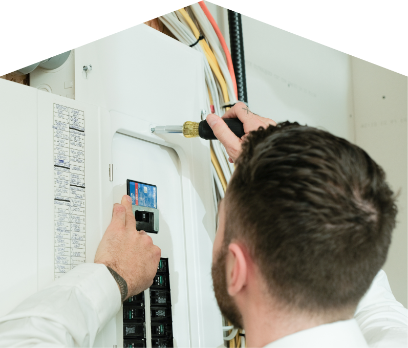Mr. Furnace electrician using a screwdriver to perform an electrical panel upgrade, working near organized wiring in a residential wall. Mr. Furnace electrician using a screwdriver to perform an electrical panel upgrade, working near organized wiring in a residential wall.