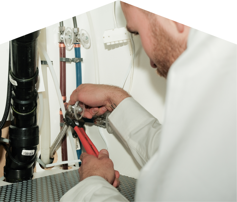 Mr. Furnace plumbing expert tightening connections under a sink during a faucet installation, surrounded by hot and cold water supply lines and PVC drainage. Mr. Furnace plumbing expert tightening connections under a sink during a faucet installation, surrounded by hot and cold water supply lines and PVC drainage.