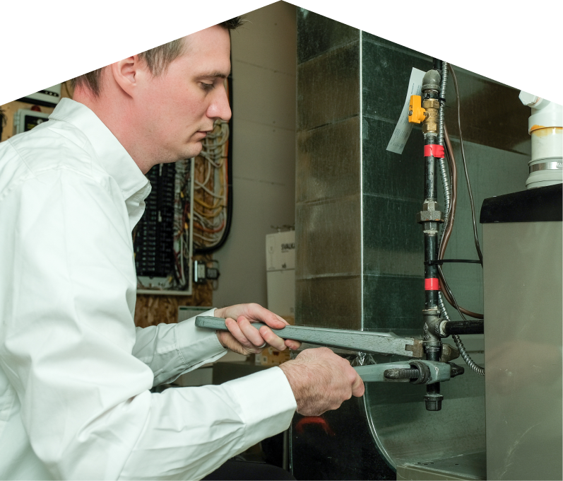 Tightening a gas line fitting with a pipe wrench, a Mr. Furnace plumbing specialist performs pipe repair beside a residential heating system. Tightening a gas line fitting with a pipe wrench, a Mr. Furnace plumbing specialist performs pipe repair beside a residential heating system.