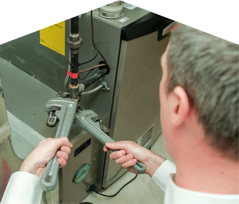 Mr. Furnace plumbing specialist using two pipe wrenches to service a gas line connection beside a residential heating unit. Mr. Furnace plumbing specialist using two pipe wrenches to service a gas line connection beside a residential heating unit.