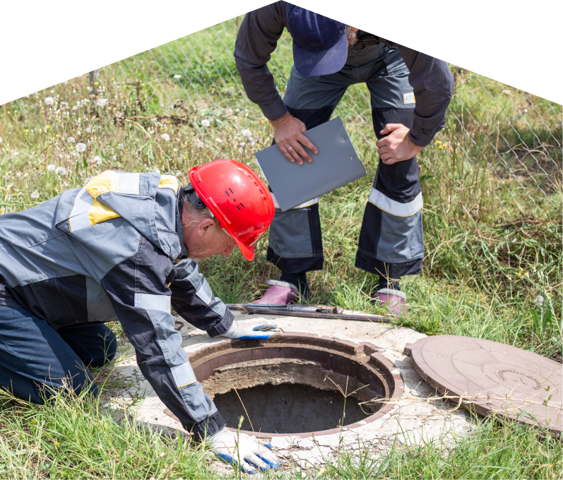 Mr. Furnace sewer crew inspecting an open manhole in a grassy field, with one member documenting findings on a clipboard. Mr. Furnace sewer crew inspecting an open manhole in a grassy field, with one member documenting findings on a clipboard.
