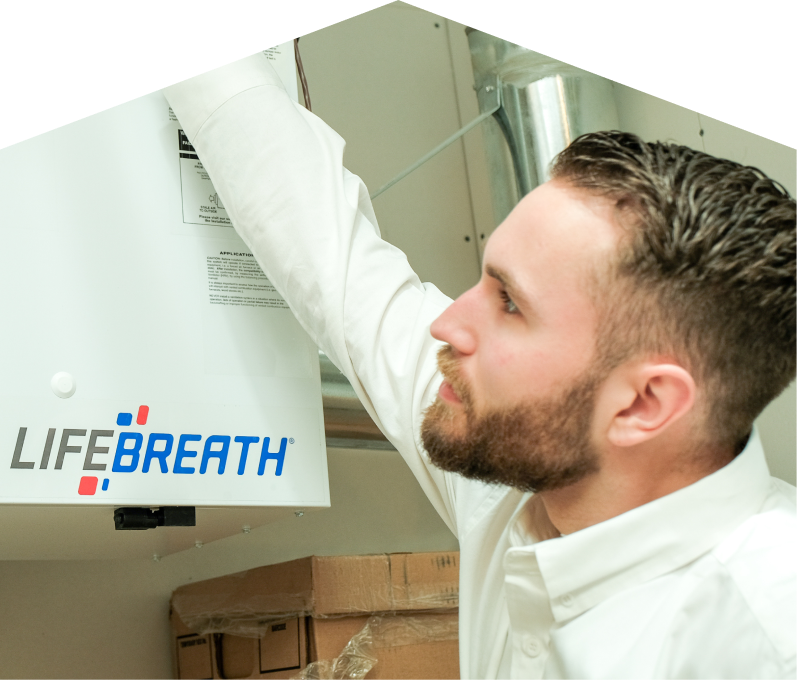Mr. Furnace indoor air quality specialist inspects a Lifebreath ventilation unit related to UV air purifiers, with ductwork and boxes in the background. Mr. Furnace indoor air quality specialist inspects a Lifebreath ventilation unit related to UV air purifiers, with ductwork and boxes in the background.