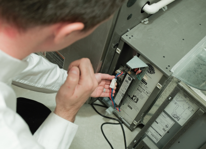 A Mr. Furnace heating technician inspecting internal wiring during a service check on a residential heating unit. A Mr. Furnace heating technician inspecting internal wiring during a service check on a residential heating unit.
