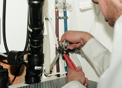 Using two pipe wrenches, a Mr. Furnace professional plumber services a pipe connection near a vertical flue or vent pipe. Using two pipe wrenches, a Mr. Furnace professional plumber services a pipe connection near a vertical flue or vent pipe.